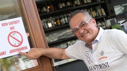 Lambros Petrou zeigt ein Schild mit der Aufschrift „Kein Eintritt mit Jogginghose“.