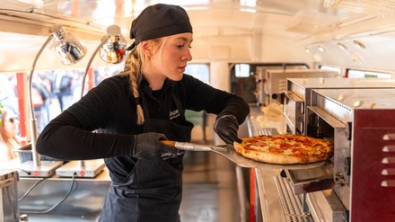 Junge Frau schiebt eine Pizza in eine Pizza-Ofen