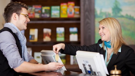Junger Mann beim Check-In im Hotel mit weiblicher Rezeptionistin