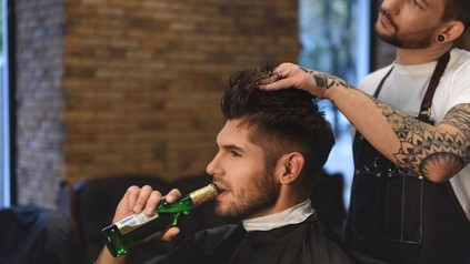 Mann trinkt Bier bei Friseur