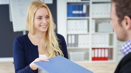Junge Frau gibt ihre Bewerbungsmappe an ihr Gegenüber