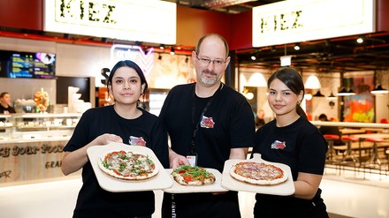 Drei Mitarbeiter präsentieren frische Pizza