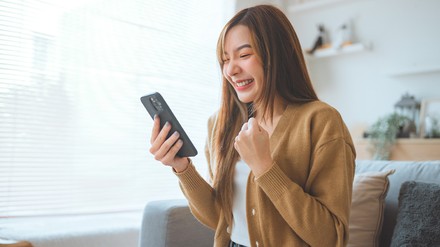 Junge Frau hält ihr Handy in der Hand und freut sich offentsichtlich