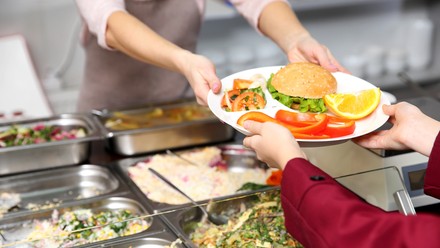 Frau gibt einer Schülerin in der Mensa Mittagessen aus.