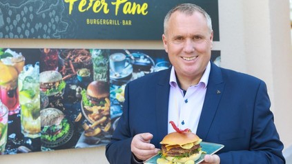 Rainer Pastätter steht mit einem Burger vor einem Peter Pane Restaurant