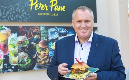 Rainer Pastätter steht mit einem Burger vor einem Peter Pane Restaurant