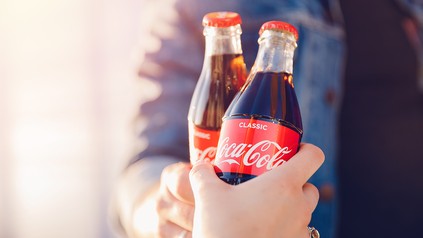zwei Menschen stoßen mit Coca-Cola Flaschen an
