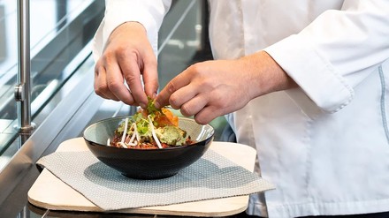 Ein Koch in weißer Haube richtet einen Salat an