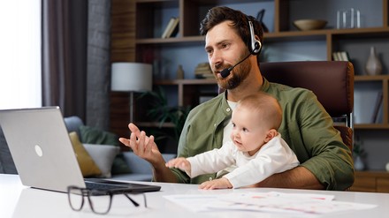 Junger Mann mit Kind auf dem Schoß während eines beruflichen Video-Calls