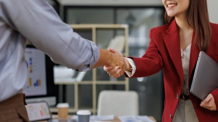 Mann und Frau in Geschäftsklamotten schütteln sich im Büro die Hände