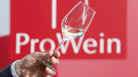 Weiswein im Glas vor roter Wand mit der Aufschrift ProWein