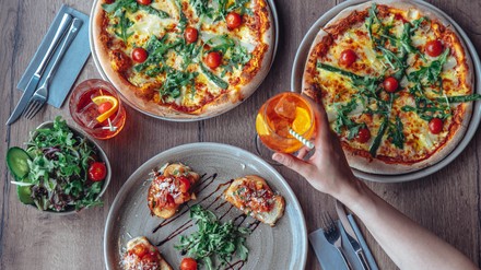 Verschiedene Pizzen und ein Glas Aperol