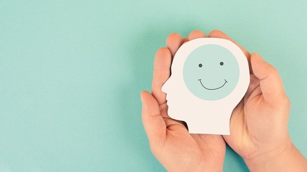 Zwei Hände halten einen symbolischen Kopf, im Gehirn ein lachender Smiley