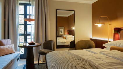 Modernisiertes Hotelzimmer im Zeller Hotel + Restaurant mit Boxspringbett, warmen Naturtönen, Holzdetails, Spiegel, Sitzbereich und indirekter Beleuchtung.