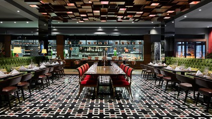 Innenansicht des Beef Grill Club by Hasir im Titanic Gendarmenmarkt Berlin mit gedeckten Tischen, roter Bestuhlung und offener Küche.