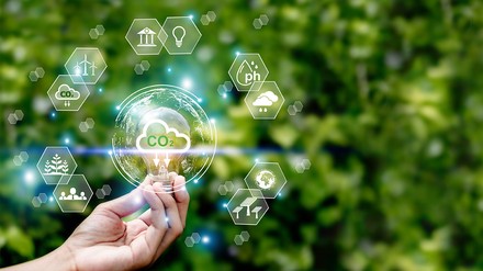 hand hält Glühbirne vor grünem Hintergrund. Glühbirne enthält Co2, außenherum Kacheln mit Klimaschutz-Symbolen