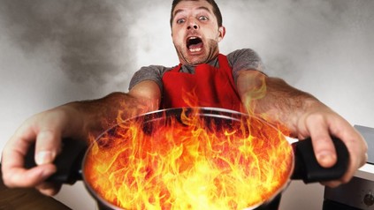 Mann hält erschreckt Topf mit Flammen von sich