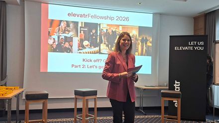 Laura Schmidt steht vor einer Präsentationsfolie „elevatrFellowship 2026“ und eröffnet den zweiten Veranstaltungstag im Arabella Alpenhotel Spitzingsee.