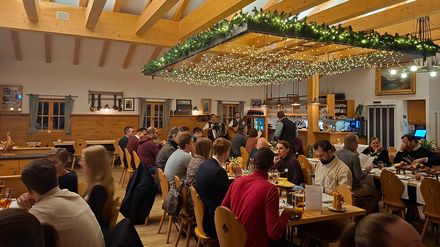 Gäste beim gemeinsamen Abendessen in der Spitzingalm mit Live-Musik, Tische im Gastraum und geselliges Beisammensein.