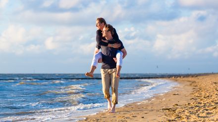 Mann trägt Frau huckepack am Strand