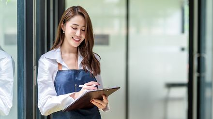 Servicekraft im Gastgewerbe mit Klemmbrett bei der Einsatz- und Schichtplanung in einem Hotel oder Restaurant.