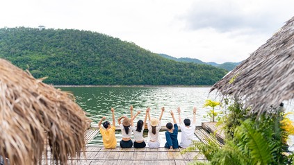 Junge Reisende der Gen Z entspannen gemeinsam auf dem Balkon eines Hauses am See in einer naturnahen Berglandschaft.
