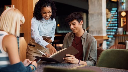 Kellnerin zeigt auf Speisekarte, die der Gast hält