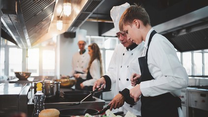Koch erklärt Auszubildenden in einer professionellen Küche Zubereitungsschritte
