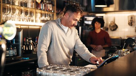 Zwei Mitarbeiter stehen mit einem Tablet an einer Bar und besprechen Abläufe im Gastronomiebetrieb.