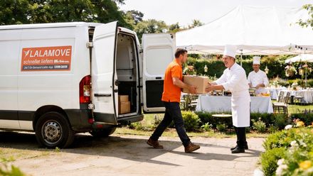 Lalamove-Lieferfahrzeug bei der Übergabe einer Lieferung an einen Koch im Außenbereich einer Veranstaltung.