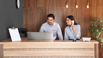 Zwei Mitarbeiter arbeiten an der Rezeption einer modernen Hotellobby.