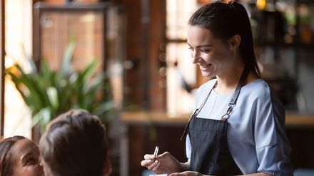 Servicekraft nimmt in einem Restaurant die Bestellung eines Gästepaares auf.