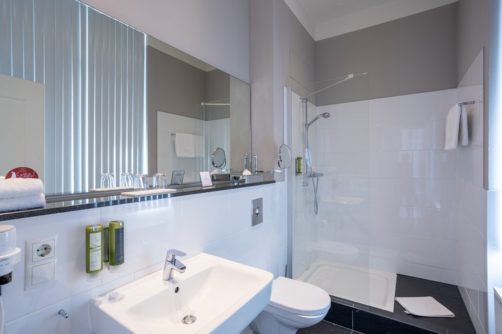 Helles Hotelbadezimmer mit Waschbecken, großer Spiegelfläche, WC und verglaster Dusche.