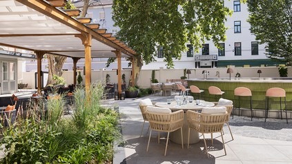 Außenbereich des Hotels Imperial Riding School in Wien mit begrünten Sitzplätzen, großen Bäumen und einer Bar.