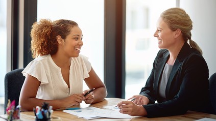 Frauen sitzen gemeinsam an einem Tisch im Büro und besprechen Unterlagen während eines persönlichen Gesprächs.