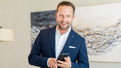 Butler und Concierge Daniel Rudolf im dunkelblauen Anzug mit einem Smartphone in der Hand.