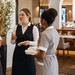 Vier Mitarbeiter aus Rezeption, Küche, Service und Housekeeping stimmen sich in einem Hotelrestaurant vor der Schicht ab.