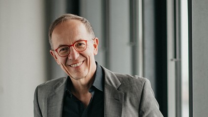 Porträt von Christian Conrad mit roter Brille und grauem Sakko in einem modernen Innenraum