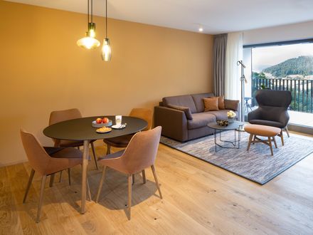 Heller Wohnbereich einer Suite der Traube Tonbach mit Sofa, Sessel, Balkon und großen Fensterfronten zum Tonbachtal