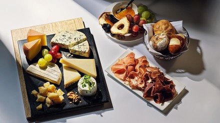 Schieferplatte mit einer Auswahl verschiedener Schweizer Käsespezialitäten, daneben ein Teller mit Wurstspezialitäten, ein Brotkörbchen und eine Fruchtschale