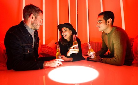 3 junge Leute mit einem Bier in der Hand über einer SAD-Lampe