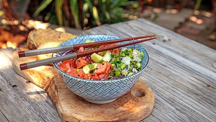 Eine Portion Pokebowl auf einem Holzbrett mit Essstäbchen