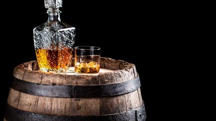Ein Whiskeyglas und eine Flasche stehen auf einem alten Holzfass