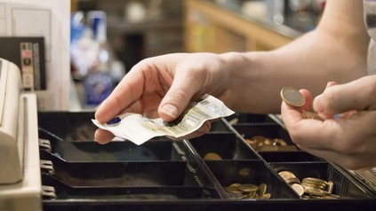 Eine Hand ordnet Geld in eine Registrierkasse ein