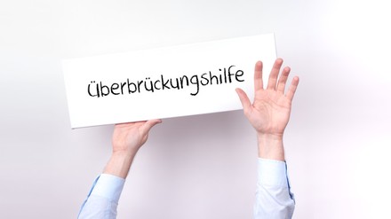 Hände, die das Schild Überbrückungshilfe hochhalten