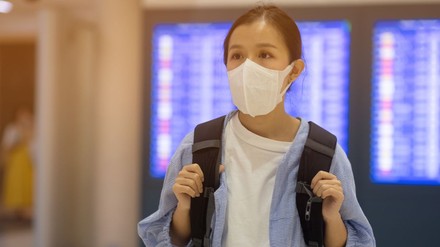 FRau mit Rucksack und Maske an einem Bahnhof