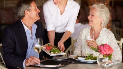 Bedienung reicht Mann Salat an Tisch
