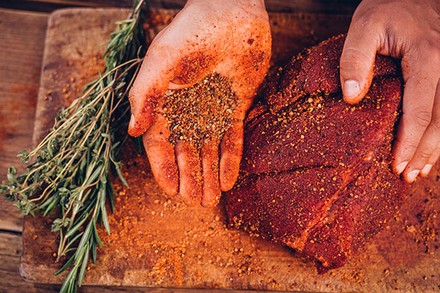 Eine Person würzt ein großes Stück Fleisch