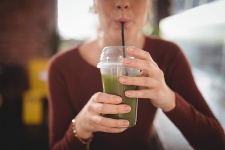 Eine Frau trinkt mit einem Trinkhalm aus einem Plastikbecher