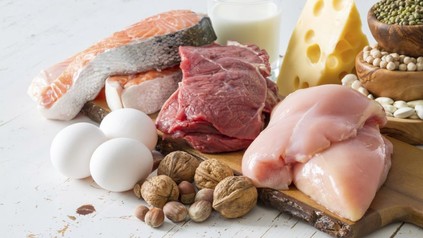 Verschiedene Lebensmittel wie Fleisch, Lachs, Eier, Nüsse und Käse auf einem Holzbrett angerichtet